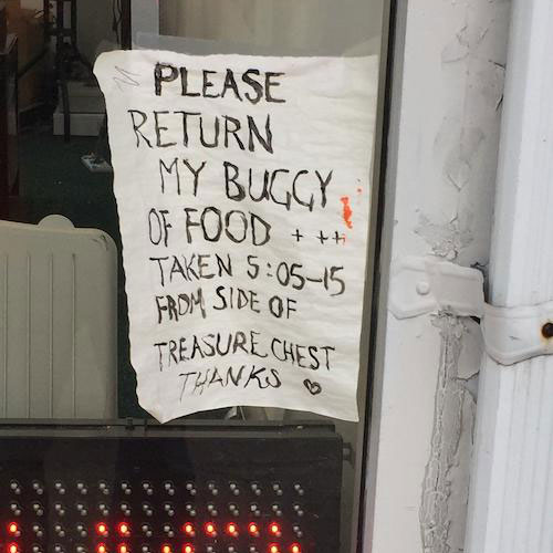 A white sign on the street, asking to return a buggy of food.