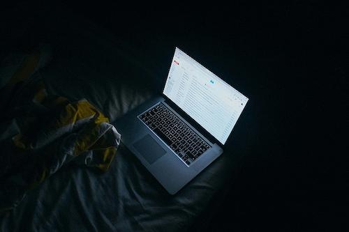 A laptop on a bed in a dark room.